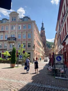 two people walking down a cobblestone street in an old european city with tall buildings