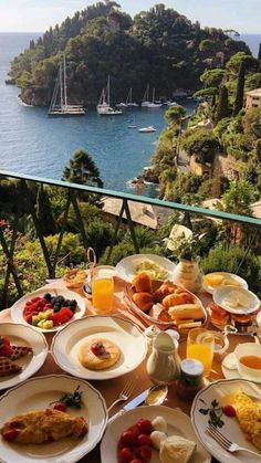 an outdoor table with food and drinks on it overlooking the water in front of some boats