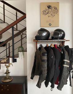 motorcycle helmets and jackets are hanging on a rack in front of a staircase with stairs