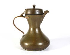 an antique brass coffee pot with a lid on a white background, the pitcher is shaped like a teapot