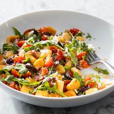 a white bowl filled with lots of food on top of a marble countertop next to a fork