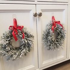 two christmas wreaths are hung on the front of white cabinets with red ribbon around them