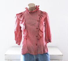 Vintage 70's gingham checked blouse.  Red and white cotton/polyester fabric.  Western, country girl styling.  Ruffled neckline and down the front.  Gathered shoulders.  Half sleeves. Condition: Good condition.  Slight piling on the fabric. Brand: Topson Downs Fabric: no fabric tag, feels like cotton/polyester Measurements: Taken flat, then doubled when necessary. Size tag: Medium Bust: 37 in. Waist: 35 in. Length: 21 in. Shoulders: 12 1/2 in. Sleeve length: 15 in. Cotton Gingham Top For Daywear, Retro Gingham Blouse For Spring, Spring Retro Gingham Blouse, Retro Fitted Tops For Picnic, Fitted Retro Tops For Picnic, Vintage Plaid Spring Tops, Vintage Plaid Top For Spring, Retro Fitted Gingham Tops, Spring Plaid Cotton Blouse