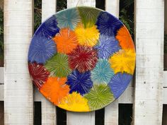 a colorful plate hanging on the side of a white fence