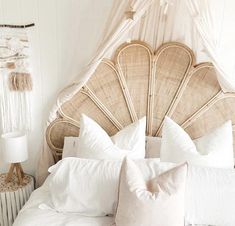 a white bed topped with pillows next to a wall mounted wicker headboard and night stand