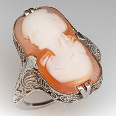 This antique filigree cameo ring features an elongated shell cameo of a woman's bust. The ring was loved and worn over the years and the cameo bust is a bit worn. The ring itself has crisp and strong details with open scroll work and milgrain. The ring is crafted in 10k white gold and is currently a size 5. The cameo is glued in for security. Luxury Cameo Wedding Rings, Ornate Cameo Jewelry For Anniversary, Antique Cameo Ring Collectible, Art Nouveau Oval Cameo Jewelry, Antique Cameo Ring Jewelry, Art Deco Cameo Ring For Collectors, Art Deco Cameo Ring Collectible, Art Deco Cameo Collectible Rings, Antique Carved Filigree Ring