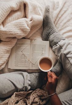 a person laying in bed holding a cup of coffee and an open book with their hands