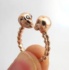 a hand holding a gold ring with two skulls on it