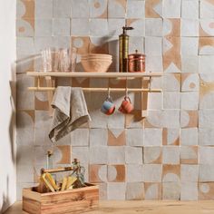 a shelf with pots, cups and tea kettles on it in front of a tiled wall