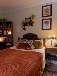 a bed with an orange blanket and pillows in a bedroom next to a book shelf