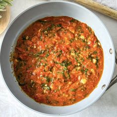 a pan filled with sauce and vegetables on top of a white table cloth next to a wooden spoon