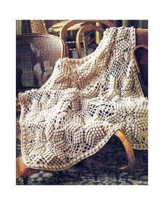 a white crocheted blanket sitting on top of a wooden chair next to chairs