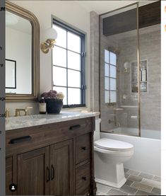 a white toilet sitting next to a bath tub in a bathroom under a window with a mirror