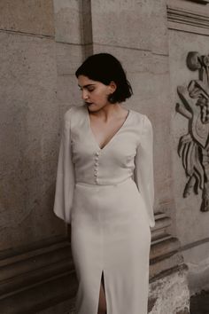 a woman in a white dress leaning against a wall