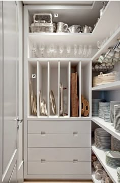 a white cupboard filled with lots of dishes and silverware next to shelves full of glasses