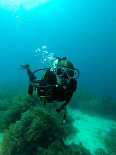 a person in scuba gear and goggles swims through the water on a coral reef