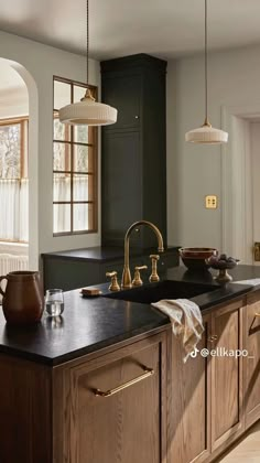 a large kitchen with wooden cabinets and black counter tops, gold faucets and hanging lights