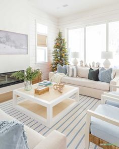 a living room filled with white furniture and a christmas tree in the window sill