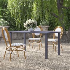 a table and chairs in the middle of a graveled area with trees behind it