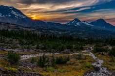 the sun is setting over some mountains with trees and water running through it, as seen from an overlook point