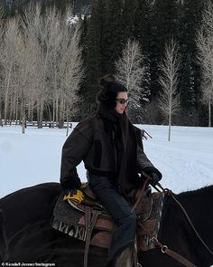 a man riding on the back of a black horse in snow covered field next to trees