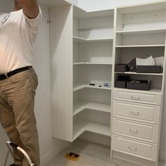 a man standing in front of a white closet with drawers and shelves on the wall