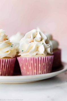 three cupcakes with white frosting and sprinkles on a plate