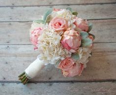 a bridal bouquet with pink and white flowers on a wooden surface, ready to be used as a bride's bouquet