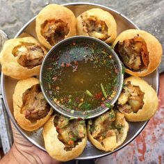 a person holding a metal plate with some food on it and dipping sauce in the middle