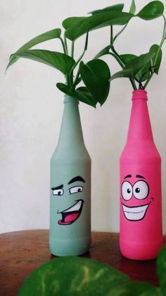 two bottles with faces painted on them sitting on a table next to a plant in a vase