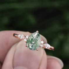 a close up of a person's hand holding a ring with a green and white stone