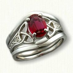 a silver ring with a red stone in the center and celtic designs on each band