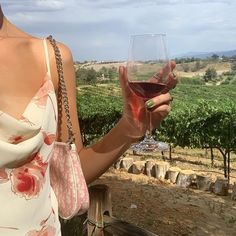 a woman holding up a glass of wine in front of some vineyards and trees