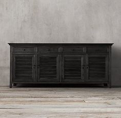 an old black cabinet with shutters on the front and bottom, against a gray wall