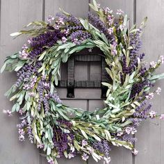 a wreath is hanging on the side of a door with purple flowers and green leaves