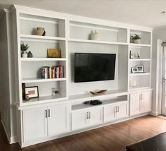 a living room with white bookcases and a flat screen tv on the wall