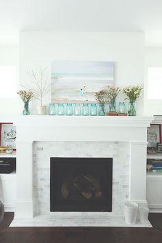 a white fireplace with vases on top of it and flowers in front of the fire place