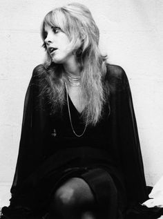 a black and white photo of a woman with long blonde hair sitting on the ground