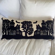 a black and white pillow sitting on top of a bed next to pillows with trees