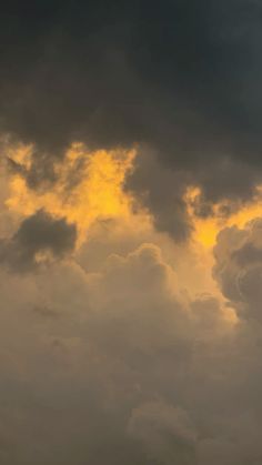 an airplane is flying in the sky with dark clouds behind it and yellow light coming from above