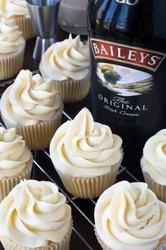 cupcakes with white frosting sitting on a cooling rack next to a bottle of bailey's