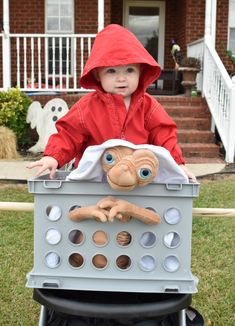 a little boy in a red jacket riding on top of a toy box with an odd face