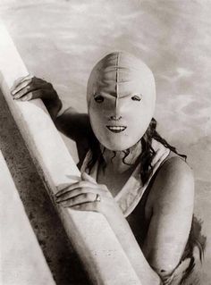 a woman wearing a mask and holding a surfboard in the water with her hands on the board