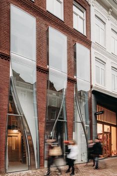 two people walking past a tall brick building with glass windows on the front and side