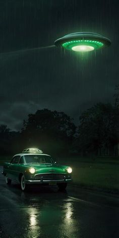 a green car driving down a rain soaked road under an alien flying saucer above it