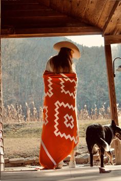 a woman wrapped in an orange blanket sitting on a porch next to a black and white cow