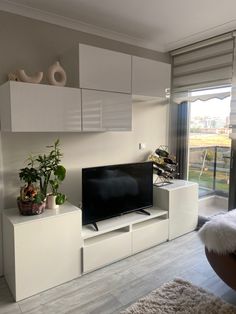 a flat screen tv sitting on top of a white entertainment center next to a window