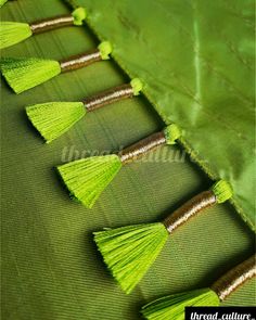 four green tassels are lined up on the side of a green fabric bag