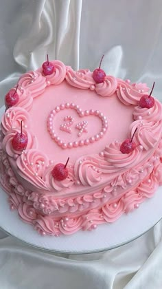 a heart shaped cake with pink frosting and cherries on top, sitting on a white table cloth