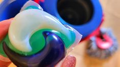 a hand holding a lollipop in front of two blue and green containers on a table